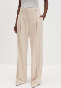 Lichtbeige wijde pantalon met een getailleerde pasvorm, voorzien van zijzakken en een vlakke voorkant. Gemaakt van een zachte stof.