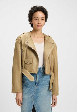 Tan leather cropped motorcycle jacket with asymmetrical zip, shoulder epaulettes, and front pocket, paired with a light blue denim skirt.