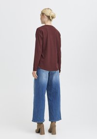 Bordeauxfarbenes Longsleeve-Oberteil kombiniert mit hellblauen weit geschnittenen Jeans. Das Oberteil hat einen runden Halsausschnitt und die Jeans haben einen leichten Used-Look sowie umgekrempelte Säume.