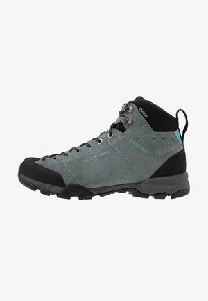 Botte de randonnée mi-haute grise et noire avec crochets pour lacets, étiquette Gore-Tex, semelle robuste et col rembourré à la cheville, conçue pour une utilisation en extérieur.