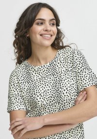 Maglietta a maniche corte in crema chiara con un motivo a macchie nere. Collo rotondo e tessuto morbido e strutturato. Fit casual.
