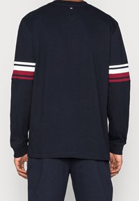Langarm-Navy-T-Shirt aus Baumwolle, mit weißen und roten Streifen an den Ärmeln, weicher Textur und einem entspannten Schnitt.