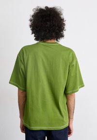 T-shirt en coton vert ample avec des manches courtes, un col rond et des détails de coutures blanches contrastantes sur les bords.