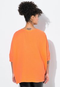 Top di un brillante arancione, dal taglio morbido e ampio, con finitura texturizzata, spalle scese e scollo rotondo. Maniche corte e orlo dritto.