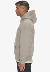 Sweat-shirt à capuche en tissu gris clair avec une poche à l'avant, coupe décontractée et poignets côtelés. Présente un logo sur la poitrine dans une teinte subtile.
