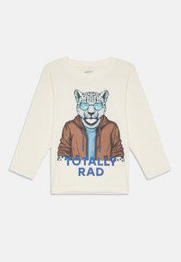 Krémová košeľa s dlhým rukávom s grafikou leoparda v slnečných okuliaroch a saku, s modrým textom "TOTÁLNE SUPER" nižšie.