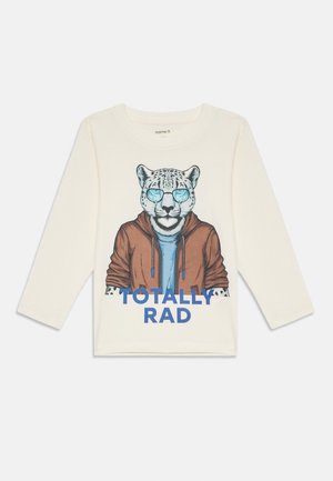 Krém színű, hosszú ujjú póló, amelyen egy napszemüveget és dzsekit viselő leopárd grafika látható, alatta pedig kék szöveg: "TOTALLY RAD".