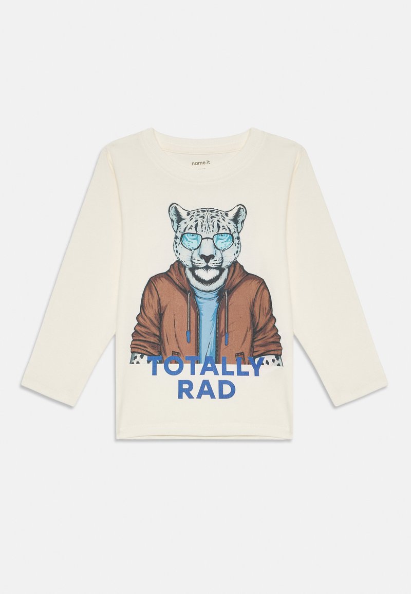Krémová košeľa s dlhým rukávom s grafikou leoparda v slnečných okuliaroch a saku, s modrým textom "TOTÁLNE SUPER" nižšie.