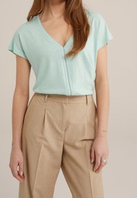 Mintgrön V-ringad topp med korta ärmar, tillverkad av mjukt tyg, kombinerad med beige högmidjade byxor med veck och en slät textur.