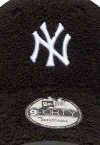 Melnā regulējamā cepure ar mīkstu, teksturētu audumu, dekorēta ar baltu izšūtu NY logotipu un apaļu sudraba New Era birku.
