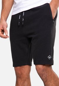 Zwarte shorts van gestructureerde stof met een elastische tailleband met trekkoord, een zijzak en een klein wit diamantlogo aan de onderkant rechts.