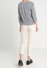 Leichte, kurzärmlige Bluse in Weiß mit schwarzem Tierdruck. Kombiniert mit enganliegenden, beigen Hosen und schwarzen Schnürschuhen.