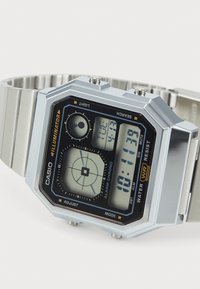 Montre Casio numérique avec bracelet en acier inoxydable argenté, cadran noir rectangulaire, affichage numérique blanc et plusieurs boutons. Résistante à l'eau.