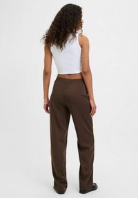 Brūni, augstiem vidukļiem un brīvā piegriezumā, bikses ar elastīgu jostu, stilizētas ar baltu īsu topu. Gluda tekstūra un minimāls dizains.