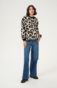 Maglione beige con stampa leopardata nera, colletto rotondo e polsini a costine, abbinato a jeans blu a gamba larga e scarpe nere.