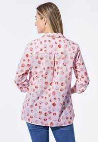 Lichtroze blouse met een cirkelvormig rood en oranje patroon. Lange mouwen, geknoopte manchetten en een rug-yoekdetail. Lichtgewicht stof.