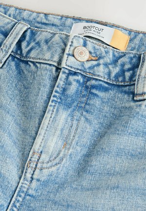 Bootcut džíny v světle modré denimové barvě, s nízkým pasem, měděným prošíváním a kovovým knoflíkem s logem. Měkká textura a zesvětlený povrch.