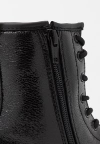 Schwarzer Leder-Stiefel mit glänzender Textur, Schnürung vorne und seitlichem Reißverschluss mit YKK-Logo als Verschluss.