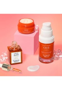 Olej do twarzy C.E.O. Glow w kwadratowej bursztynowej butelce, obok nawilżającego kremu C.E.O. w okrągłym pomarańczowym pojemniku i serum rozświetlającego C.E.O. Kryształowe akcenty.