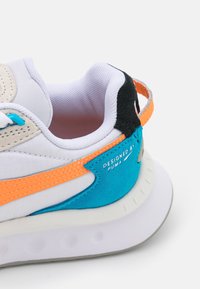 Sneaker bianco con tomaia in tessuto, dotato di accenti blu e arancioni, dettagli in suede e una suola bianca texturizzata.