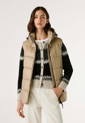 Beige padded vest with a hood, featuring a zip front and black and gray patterned knit sweater underneath, paired with light-colored pants.