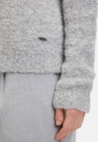 Helles graues, strukturiertes Pulli mit einem flauschigen Strickstoff. Verfügt über ein Logo-Detail und gerippte Ärmelbündchen. Kombiniert mit hellgrauen Hosen.