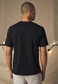 Sort bomulds T-shirt med klassisk pasform, korte ærmer og rund hals, vist fra ryggen, parret med lyse bukser.