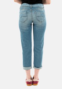 Jeans in denim blu chiaro con una vestibilità leggermente affusolata, due tasche posteriori e orli arrotolati, indossati con scarpe rosse e beige.