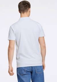 Camisa polo de color azul claro con una textura suave y mangas cortas, combinada con unos jeans de mezclilla azules. Costuras visibles en las mangas y el dobladillo.