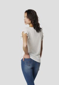 Chemise blanche à manches courtes avec un ourlet à volants, associée à un jean bleu ajusté doté de coutures décoratives sur les poches arrière.