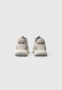Beige SportSneakers mit grauem Akzent, strukturiertem Obermaterial, gepolsterter Sohle und Zuglasche hinten. Mit einem Logo-Detail.