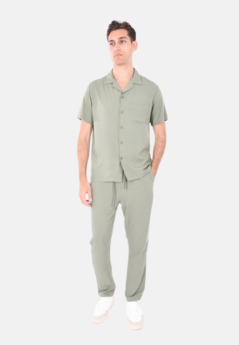 Maglietta verde chiaro a maniche corte con taschino, abbinata a pantaloni coordinati con vita elasticizzata e vestibilità comoda, completata da scarpe bianche.