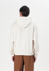 Hoodie in lichtbeige met een relaxte pasvorm. Ribgebreide manchetten en zoom, zachte stoftextuur en minimale naaddetails.