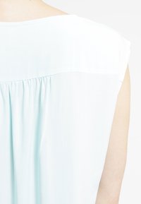 Top azzurro chiaro con vestibilità rilassata, scollatura a barca e dettagli plissettati sul retro. Realizzato in tessuto morbido e leggero.