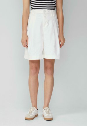 White cotton shorts with a wide-leg design, featuring a waistband with loops and side pockets. Paired with light-colored sneakers.