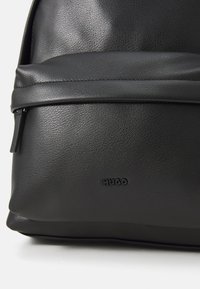 Zaino in pelle nera testurizzata con una tasca con zip e logo "HUGO" impresso al centro inferiore.