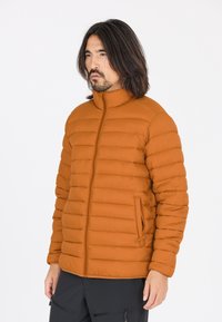 Orange puffjacka med hög krage, horisontell quiltning, sidofickor och en slät yta, kombinerad med mörka byxor.