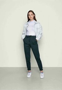 Uma jaqueta de ganga azul clara sobre uma t-shirt branca, combinada com calças de jogging verde escuras e sapatilhas brancas. Simples, com um ajuste descontraído; sem padrões.