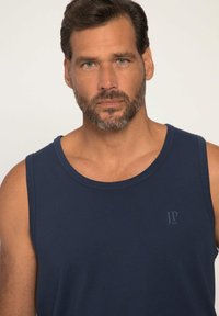 Granatowy bezrękawnik wykonany z miękkiego materiału, z okrągłym dekoltem i subtelnym logo na klatce piersiowej. Gładka faktura i dopasowanie.