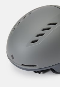 Casco de ciclismo gris con un acabado suave y mate. Cuenta con ranuras de ventilación y correas ajustables para un ajuste seguro. Forma redondeada.