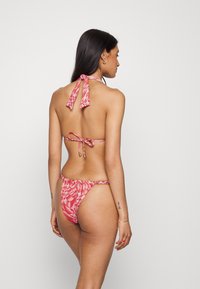 Biquíni halter com padrão vermelho, com laços no pescoço e nas costas, apresentando uma parte de baixo de cintura baixa e um design floral em tecido suave.