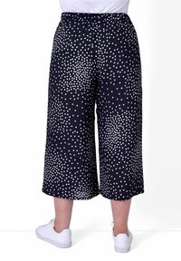 Czarne kuloty w biały wzór w kropki, elastyczny pas, lekki materiał, długość do kostek, w połączeniu z białymi sneakersami.