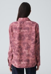 Chemise à manches longues, rose pâle, avec un motif tie-dye, dotée d'un col et de poignets boutonnés, fabriquée dans un tissu doux et texturé.