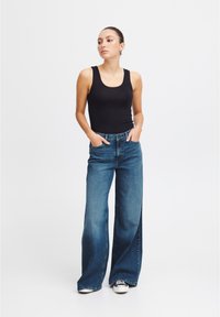 Top nero abbinato a jeans a gamba larga di un azzurro chiaro. I jeans hanno un lavaggio sbiadito e due tasche frontali. Il modello indossa sneakers bianche.