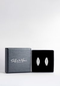 Silverörhängen med en texturerad, oval design prydd med små klara stenar, presenterade i en svart sammet-fodrad låda med metallisk finish.