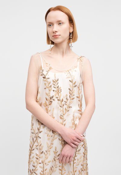 Αμάνικο, διάφανο φόρεμα σε κρεμ απόχρωση με κεντήματα από φύλλα χρυσού. Διαθέτει λεπτές τιράντες και διακριτικές, λαμπερές λεπτομέρειες. Κομψός, ρέων σχεδιασμός.