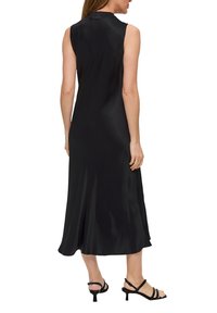 Czarna sukienka bez rękawów z wysokim kołnierzem, gładkiego satynowego materiału, o długości do kolan, zapinana z tyłu na zamek. W zestawie z czarnymi sandałami na obcasie.