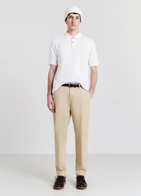 Weißes kurzärmliges Poloshirt mit drei Knöpfen, beige Hose und dunkle braune Schuhe, ergänzt durch eine gerippte weiße Mütze.