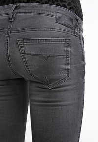 Vaqueros de mezclilla grises con un diseño ajustado, que presentan un bolsillo trasero en forma de V y un sutil desgaste. Tejido texturizado con un acabado elegante.