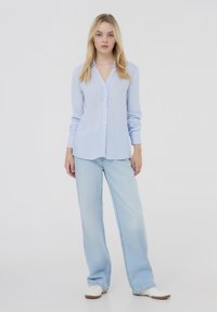 Camicia a maniche lunghe azzurro chiaro con strisce bianche verticali, con bottoni, abbinata a jeans in denim chiaro a vita alta e sneakers bianche.